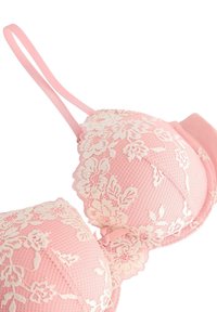 Lichtroze beha met kanten overlay en bloemmotieven, gewatteerde cups en verstelbare banden. Gladde stof met delicate accenten.