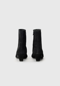 Bottines en suède noir avec un talon effilé, présentant une fermeture éclair à l'arrière et une surface lisse et texturée.