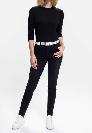 Top nero a maniche lunghe abbinato a jeans skinny neri e una cintura intrecciata bianca. Completa il look un paio di sneakers bianche, creando un outfit monocromatico.