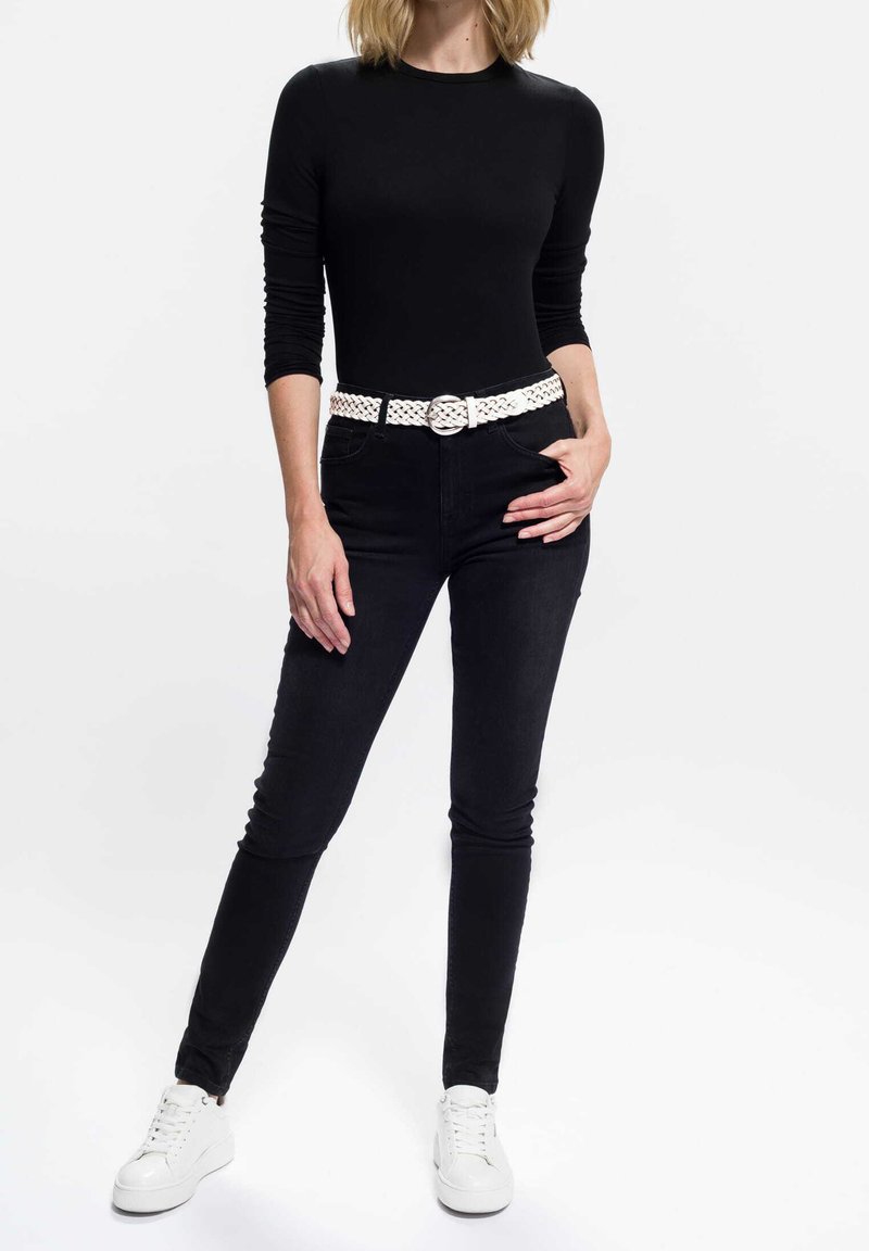 Sort langærmet top kombineret med sorte skinny jeans og et hvidt flettet bælte. Hvide sneakers fuldender outfittet og skaber et monokromt look.