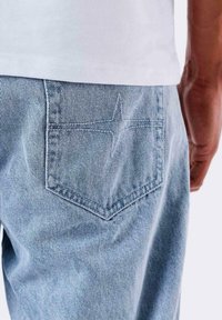 Jeans de mezclilla azul claro con un bolsillo trasero que presenta un detalle de costura en forma de estrella. El material parece suave, con un aspecto clásico y ligeramente desgastado.
