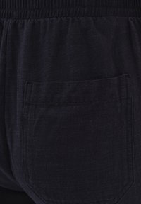 Dunkelblaue Hose mit einem gerafften Bund und einer einzigen Gesäßtasche mit detaillierter Steppnaht. Glatte Textur mit einem subtilen Gewebe-Muster.