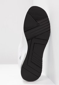 Zwarte rubberen schoenzool met geometrische loopvlakpatronen, weergegeven tegen een witte achtergrond, gezien vanaf de onderkant.