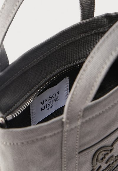 Γκρι υφασμάτινη τσάντα ώμου με εμφανές εσωτερικό τσεπάκι με φερμουάρ που φέρει άσπρη ετικέτα με την επιγραφή "Maison Kitsuné Paris".