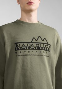 Felpa verde oliva con collo a girocollo a coste, caratterizzata da un logo stampato in nero "NAPAPIJRI geographic" e un design montano sul davanti.