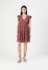 Ruffled sleeve dress in mauve, featuring eyelet detail, a v-neckline, and an elastic waist. Paired with strappy beige sandals.