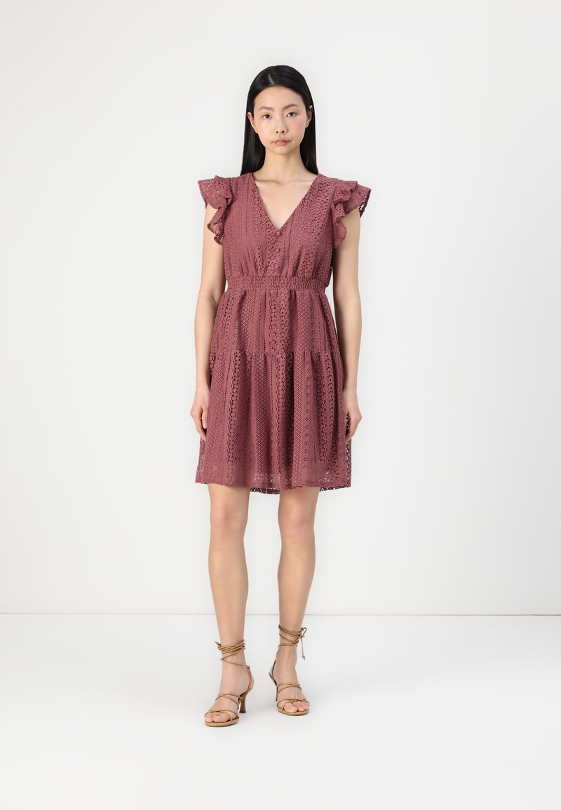 Ruffled sleeve dress in mauve, featuring eyelet detail, a v-neckline, and an elastic waist. Paired with strappy beige sandals.