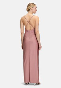 Robe longue sans manches en satin rose doux avec une silhouette ajustée, des bretelles croisées dans le dos et une fermeture éclair sécurisée à l'arrière.