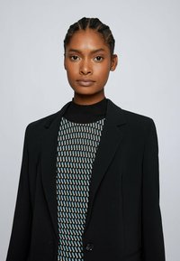 Black blazer with a structured design, notched lapels, and a single button. Underneath, a patterned top with blue and beige elements.
