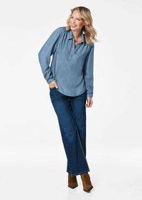 Hellblaues Jeanshemd mit Kragen, langen Ärmeln und abgerundetem Saum, kombiniert mit dunkelblauen Jeans und braunen Stiefeletten.