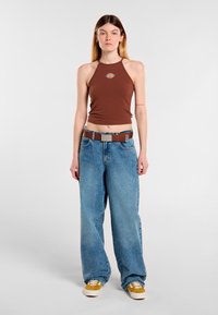Hnědý halter top s logem, světle modré vysoké volné džíny a žluté tenisky s bílou podrážkou; hladký materiál a uvolněný střih.
