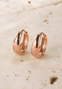 Orecchini a cerchio in oro rosa con una superficie liscia e lucida, caratterizzati da una forma arrotondata e un design con chiusura aperta per una facile vestibilità.