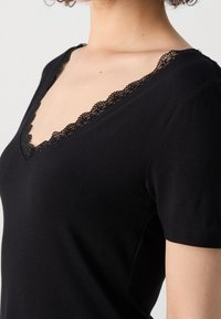 Femme portant un haut noir à manches courtes avec un col en V bordé de délicates dentelles noires.