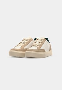 Sneakers con una toma in suede beige e pelle crema, dettagli verdi sul tallone, punta rotonda e suola in gomma piatta. Design con lacci.