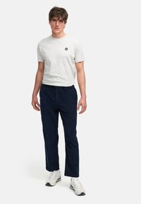 Lys grå crew neck t-skjorte med en liten marineblå logo; kombinert med marineblå kordfløyelsbukser; modellen har på seg hvite sneakers med grå detaljer.