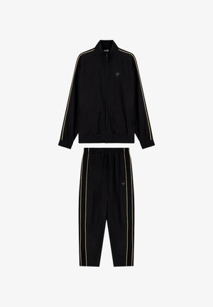 Tuta nera in tessuto strutturato, con strisce dorate lungo le braccia e le gambe, e polsini elastici su giacca e pantaloni.