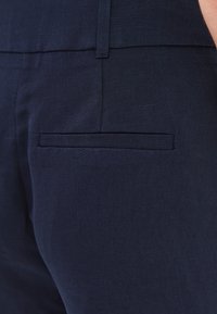 Tmavě modré lněné kalhoty s hladkou texturou, které mají skrytou zadní kapsu a čistý design pasu.