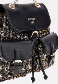Zaino in pelle nera e tweed multicolore con tracolle e fibbie in metallo dorato, logo "GUESS girl" sulla chiusura a patta.