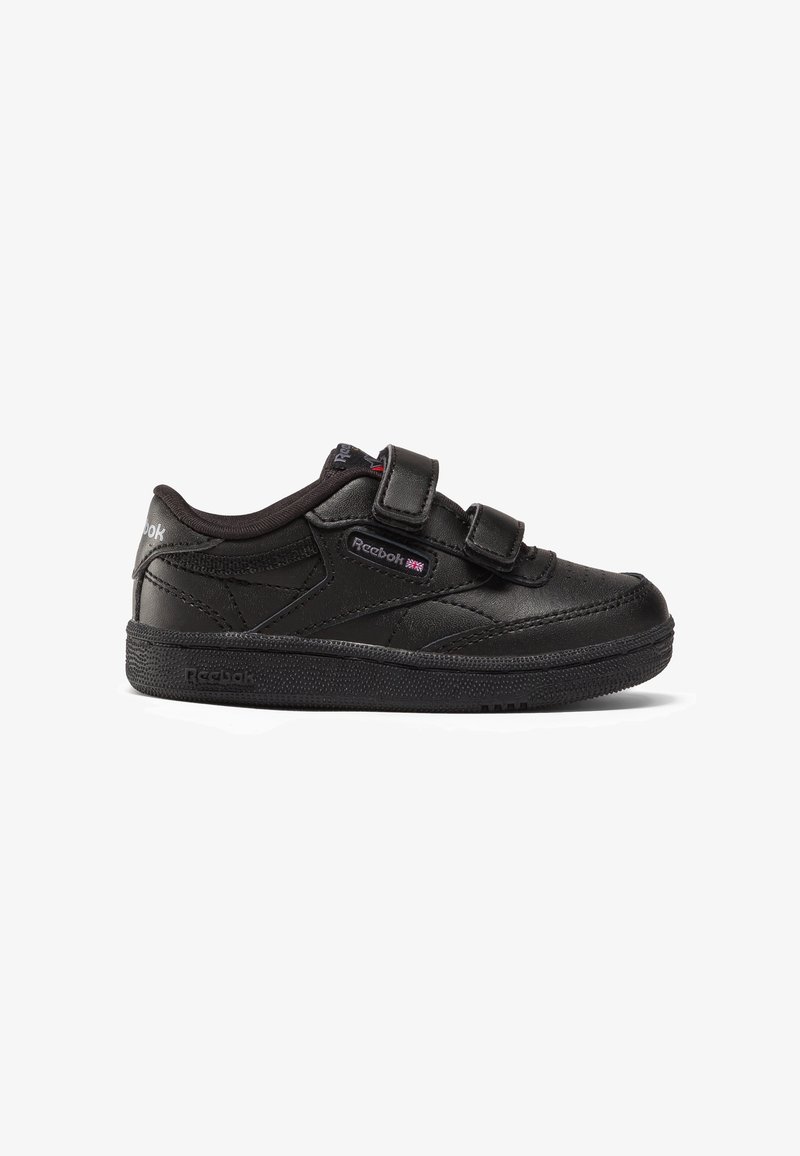 Baskets noires Reebok avec deux bandes Velcro ajustables, semelle texturée, et logo Reebok avec un petit drapeau britannique sur le côté.