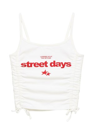 Biały skręcany crop top na cienkich ramiączkach z czerwonym napisem "looking up at the skyline street days" i dwoma czerwonymi gwiazdkami poniżej napisu.