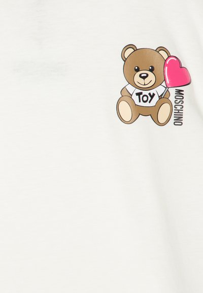 White t-shirt featuring a cartoon bear with a heart-shaped balloon, labeled "TOY." The bear has brown fur and a simple, playful design.