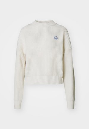White ribbed knit sweater with a high neck and dropped shoulders. Features a small blue smiley logo on the chest. Cropped design.