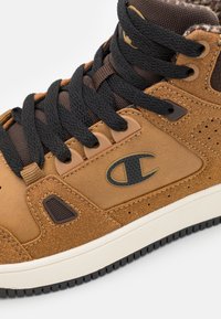 Brązowe zamszowe sneakersy high-top z czarnymi sznurówkami, akcentami z teksturowanej tkaniny, perforacjami i wyraźnym logo po boku.