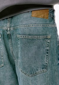 Svijetloplavi traperice s teksturiranom površinom, koje sadrže dva stražnja džepa i smeđi kožni oznaku na struku.