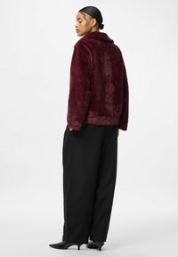 Bordeaux faux fur jakke med krave, afslappet pasform og lange ærmer, parret med sorte brede bukser og spidse sorte sko.