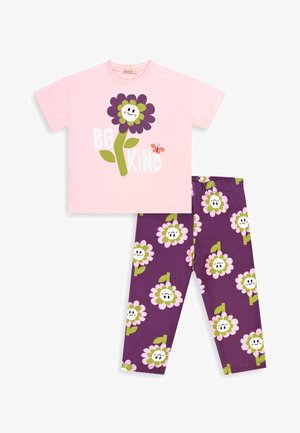 Lasten pyjamapuku, jossa vaaleanpunainen lyhythihainen paita, jossa hymyilevä violetti kukka ja teksti "Ole kiltti", yhdistetty violetteihin housuihin, joissa on hymyileviä kukkia.