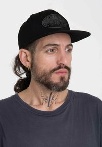 Black baseball cap featuring a raised black Batman logo on the front, worn with a gray T-shirt, showcasing a butterfly tattoo on the neck.