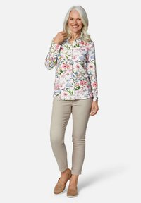 Blumiges Button-Up-Hemd mit rosa, blauen und grünen Mustern; lange Ärmel; mit Kragen. Kombiniert mit beigen Hosen und hellbraunen Schuhen.