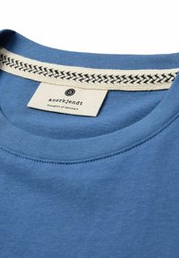 Tricou din bumbac albastru cu guler rotund. Gulerul prezintă un accent țesut în nuanțe de bej și negru. Eticheta scrie "anerkjendt thoughts of denmark."