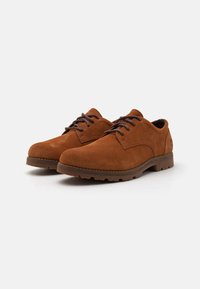 Chaussures en suède marron à lacets avec un bout arrondi, semelle en caoutchouc marron contrastante et détails texturés sur le dessus. Présente un design cousu.