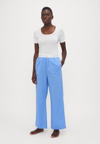Witte korte mouwen t-shirt gecombineerd met lichtblauwe wijde broek met elastische tailleband en Calvin Klein-logo op de band.