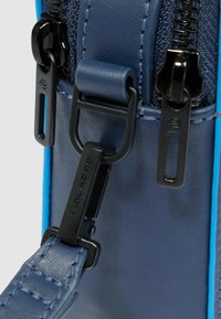 Dettaglio di borsa in pelle blu e blu navy con hardware in metallo nero, doppi cerniere e tracolla texturizzata con dettagli di cuciture.
