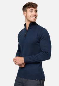 Mornarice plavi zip-up džemper s rebrastim ovratnikom i manžetama, napravljen od glatkog pletenog materijala, s delimičnim zatvaračem na vratu.