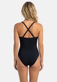 Sort badedragt i ét stykke med krydsede stropper på ryggen, glat tekstur og benudskæring med høj kant. Har minimal detaljering.