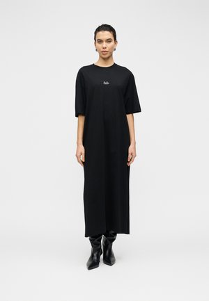 Sort bomulds maxikjole med korte ærmer, rund halsudskæring, lige snit og lille logodetalje på brystet. Modellen har sorte ankelstøvler på.