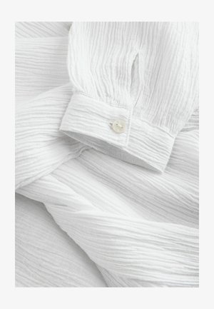 Bluză albă texturată, cu un model crepat, mânici bufante și închidere cu buton, având un finisaj neted, perlă.