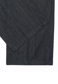 Tissu en denim gris foncé montrant des jambes de pantalon qui se chevauchent avec des coutures visibles et des détails d'ourlet sur un fond blanc.