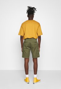 Pantalones cortos de cargo caqui con bolsillos laterales, combinados con una camiseta amarilla mostaza y zapatillas altas amarillas. Calcetines blancos visibles.