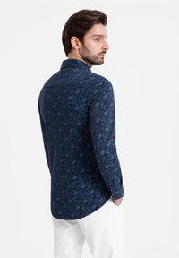 Marineblauwe blouse met lange mouwen, voorzien van een ingewikkeld bloemenpatroon, met knoopsluiting bij de kraag en manchetten, gemaakt van lichte stof.