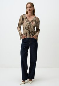 Bluse mit floralem Muster und Rüschenausschnitt in V-Form, kombiniert mit hochgeschnittenen dunklen Jeans und spitzen weißen Absätzen.