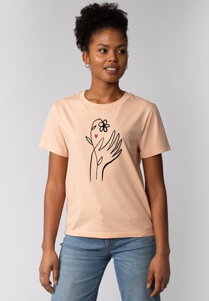 Perzikkleurige katoenen t-shirt met korte mouwen, voorzien van een zwart lijntekening ontwerp van handen, een bloem en een hart aan de voorkant.