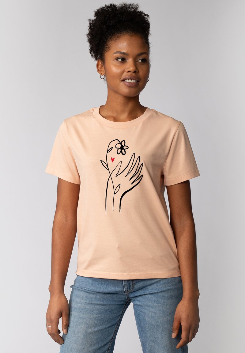 T-shirt en coton pêche à manches courtes avec un design en ligne noire représentant des mains, une fleur et un cœur sur le devant.