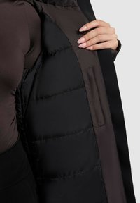 Czarna kurtka puchowa z kontrastowym ciemnym wnętrzem. Charakteryzuje się gładką teksturą i boczną kieszenią widoczną wewnątrz kurtki.