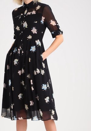 Mustakuvioinen mekko, jossa on napitettava etuosa, lyhyet käännetyt hihat, läpikuultava kangas ja virtaava hame, jossa on pastellisia kukkakuoseja.