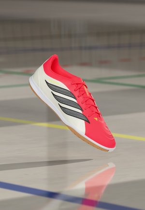 Chaussure de sport rouge et blanche avec une tige texturée, arborant trois rayures noires et une semelle en caoutchouc. Les lacets sont d'un rouge vif, mettant en valeur le design.