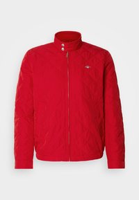 Giacca trapuntata rossa con colletto alto, chiusura frontale con zip e bottoni a pressione. Presenta tasche laterali e un dettaglio con logo sul petto.